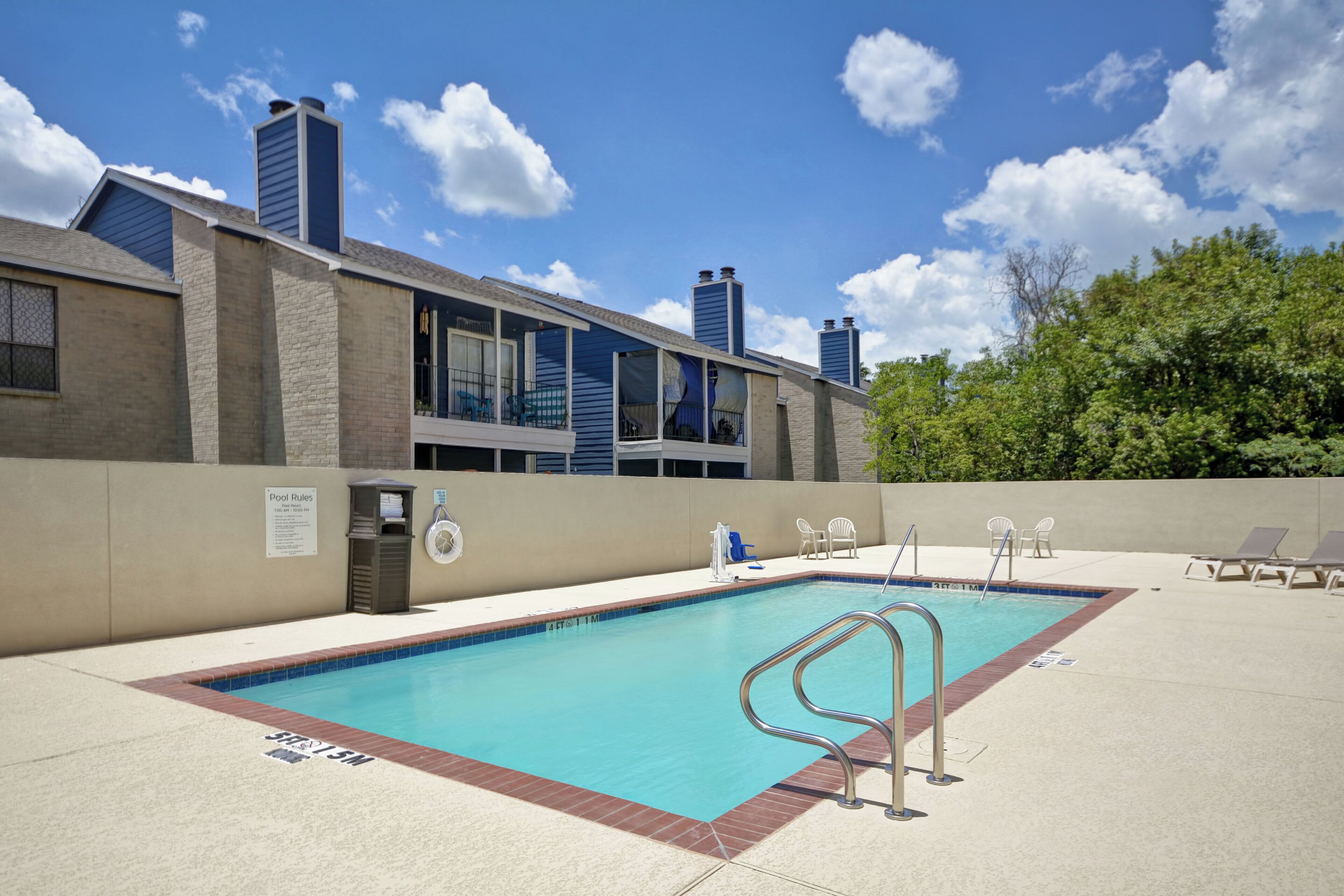 A swimming pool with a lifeguard stand, lounge chairs, and a sign indicating pool rules.