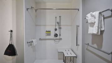 A walk-in shower with a glass door, a towel rack with towels, a small table, and a grab bar.