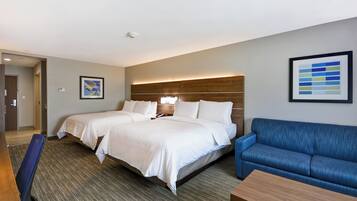 Une chambre d’hôtel avec deux lits, un canapé bleu, un bureau en bois et un tableau abstrait encadré accroché au mur.