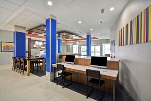Un espacio de oficina moderno con mostrador de recepción, computadoras y una mesa de reuniones con sillas.