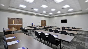 Una sala de conferencias con varias mesas, sillas y una pantalla de televisión.