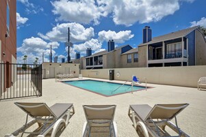 Zona de piscina con sillones de descanso, una valla delimitando la piscina y un edificio con varias ventanas y balcones al fondo.