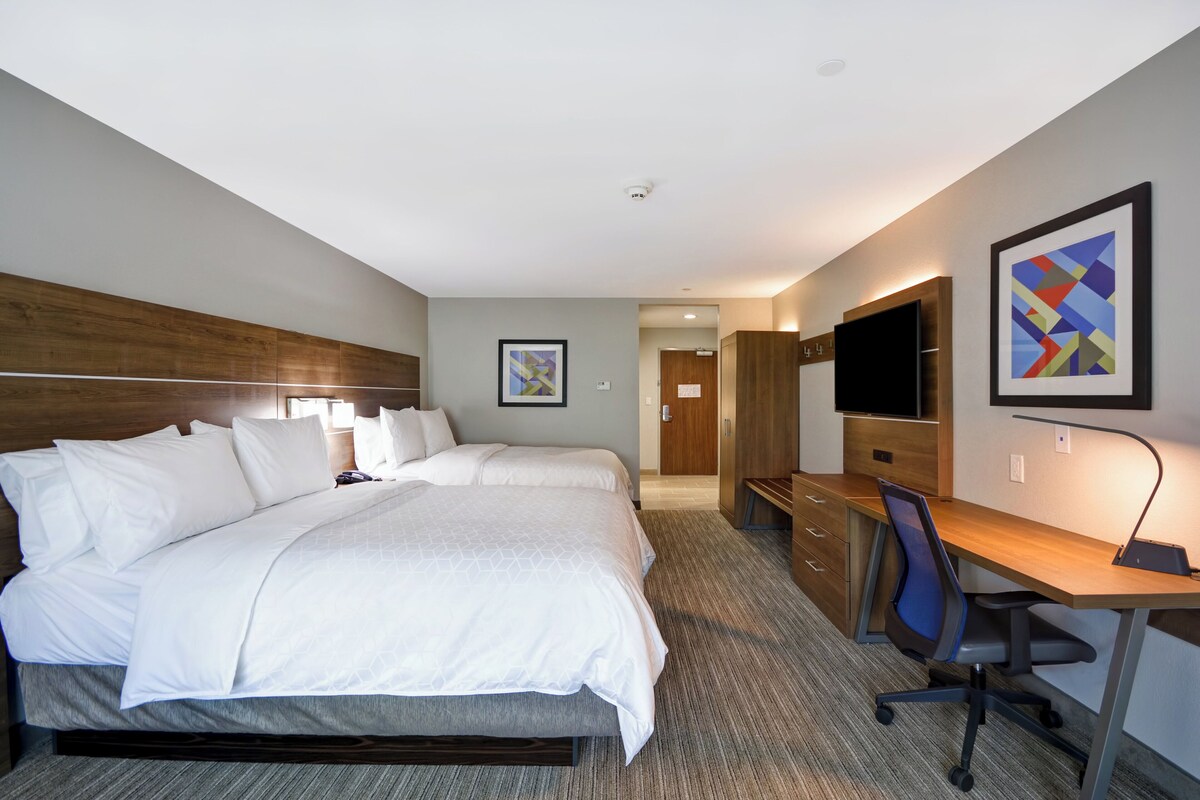 A hotel room with a large bed, a desk with a chair, a TV, and artwork on the wall.