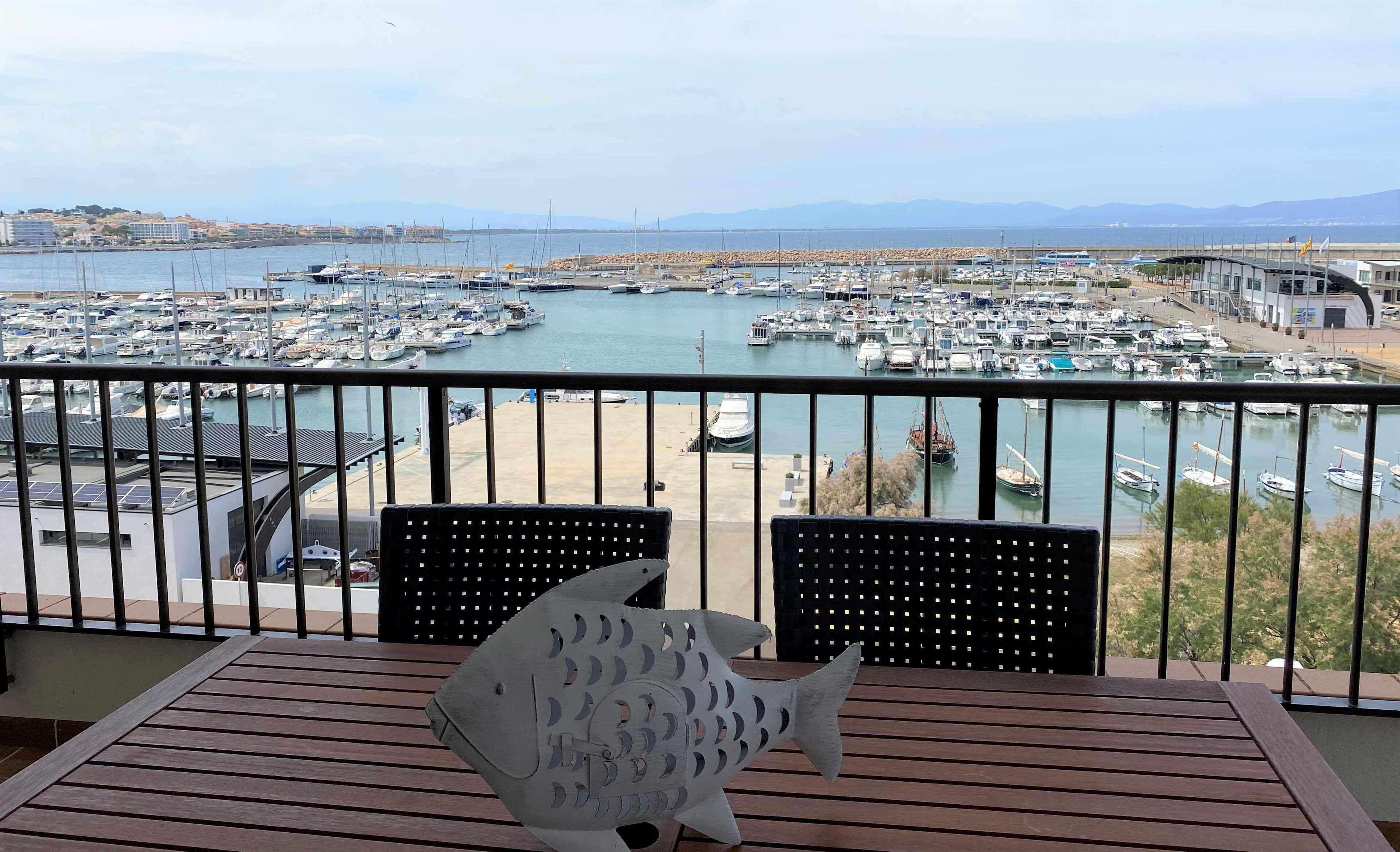 Uma varanda com vista para uma marina repleta de barcos, uma ponte ao longe e montanhas.