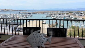Un balcon offrant une vue sur une marina remplie de bateaux, un pont situé au loin et des montagnes.