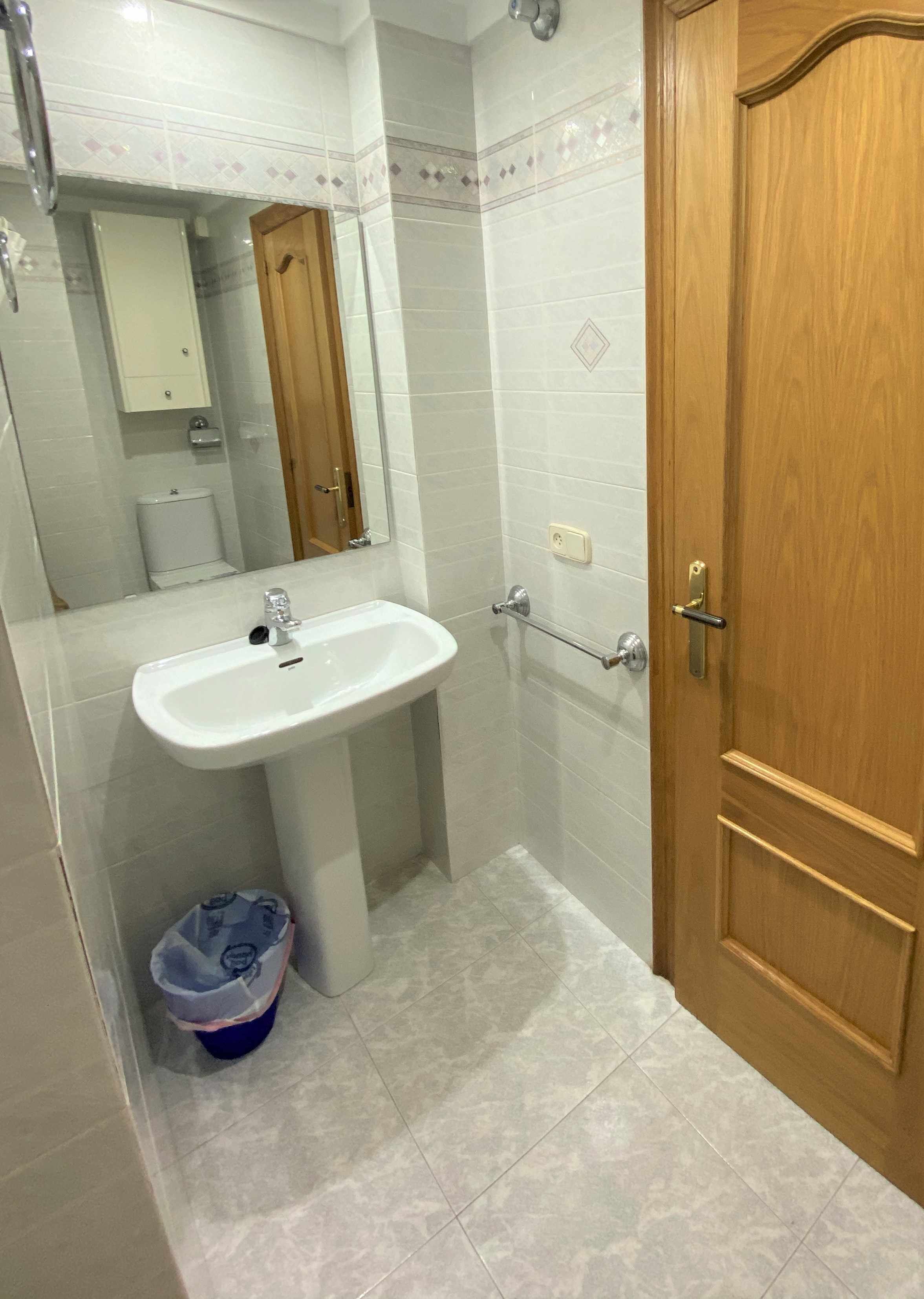 A bathroom with a white sink, a wooden door, and a mirror.