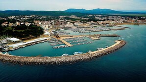 Vue aérienne d’une ville côtière avec un port de plaisance, des immeubles résidentiels et des montagnes en arrière-plan.