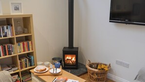 Een gezellige woonkamer met een boekenkast, een tafel met een tijdschrift, een open haard en een aan de muur bevestigde televisie.