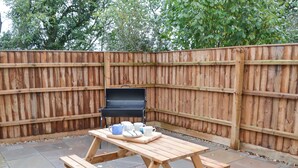 Een houten barbecue en picknicktafel, geplaatst voor een houten omheining in een buitenruimte.