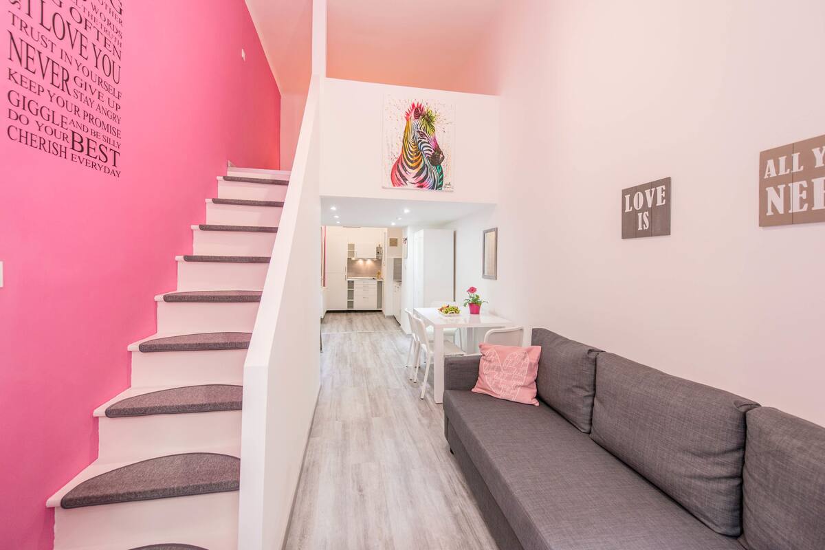 A modern interior with a staircase, a grey sofa, and motivational wall art.
