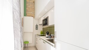 A modern kitchen with white cabinets, a microwave, a coffee maker, and a green stool. - happy home Budapest FOX (Budapest)