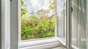 A window with a view of a lush green garden and a building in the background. - happy home Budapest FOX (Budapest)