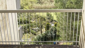 Un balcon doté d’une rambarde en métal, donnant sur un jardin avec des arbres et une pelouse.