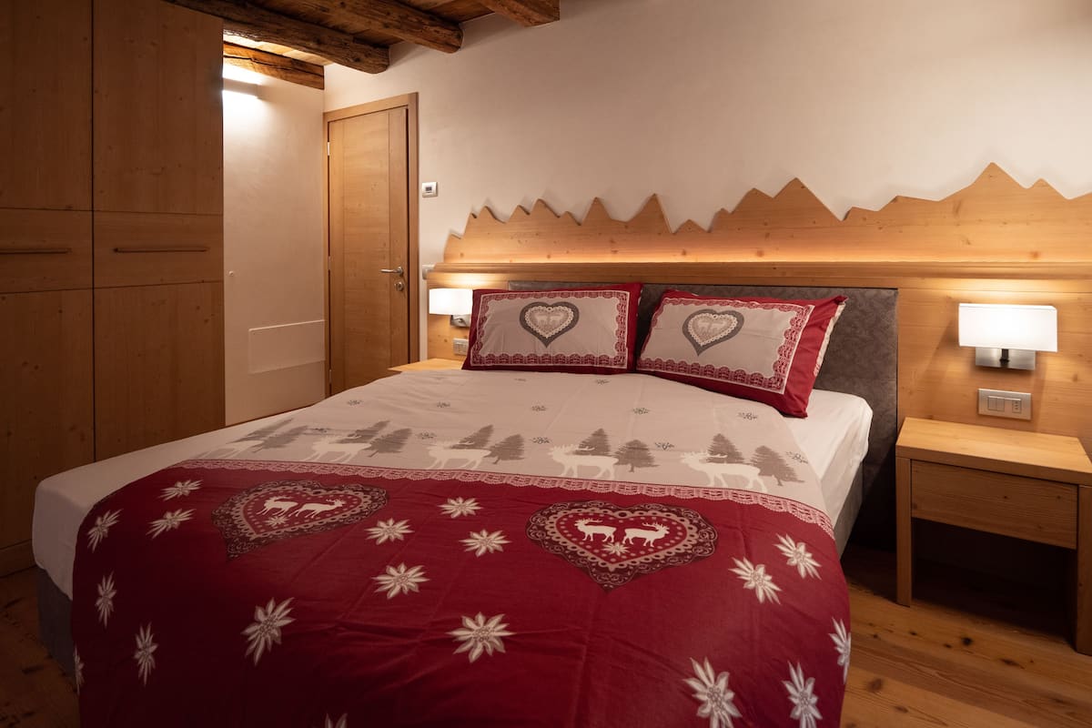 Ein Schlafzimmer mit einem hölzernen Kopfteil, einem Bett mit einer rot-weißen Bettdecke, zwei herzförmigen Kissen und einem Nachttisch mit einer Lampe.
