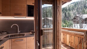 Eine moderne Küche mit Holzschränken, einer Edelstahl-Spüle und einer Glastür, die auf einen Balkon mit Holzgeländer führt.