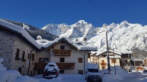 Ein verschneites Bergdorf mit traditionellen Holzhäusern, einem Steinhaus und einem geparkten Auto davor.
