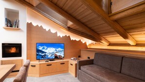 Ein gemütliches Wohnzimmer mit Kamin, Fernseher, einer Couch und einer Holzbalkendecke.