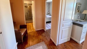 A room with a wooden floor, a chair, a bed, a bathroom with a shower, and a mirror. - Olive Tree, Superb gîte, Heated Pool near Carcassonne, overlooking Canal du Midi (Marseillette)