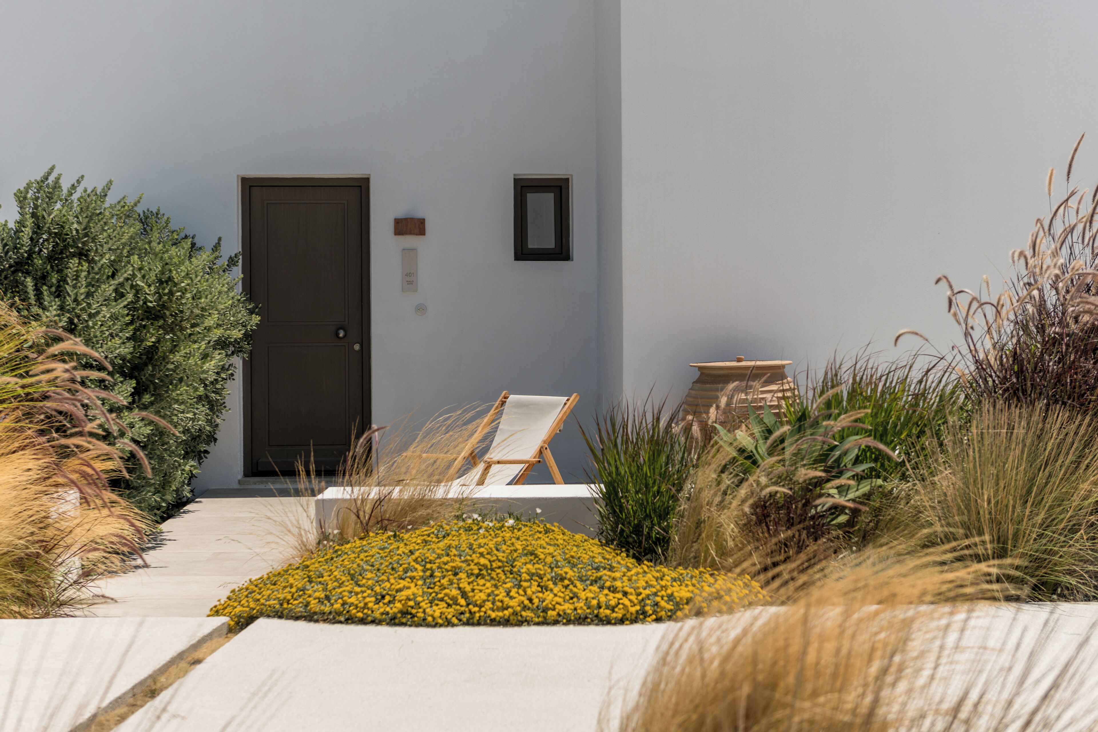 Un bâtiment moderne avec une porte sombre, un petit tableau encadré et une chaise blanche à l’extérieur.