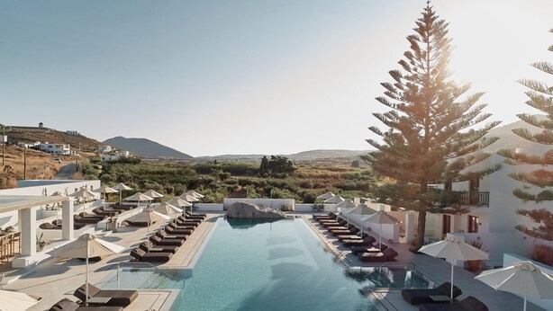 Un espace piscine doté de chaises longues et de parasols, entouré de verdure et avec une chaîne de montagnes en toile de fond.
