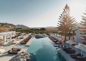 A pool area with lounge chairs and umbrellas, surrounded by greenery and a mountainous backdrop. - Parilio, a Member of Design Hotels (Paros)