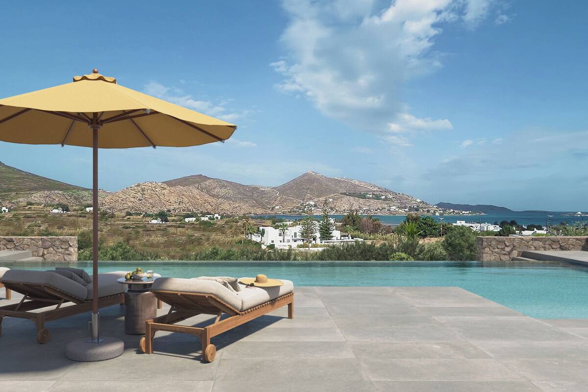 A poolside area with lounge chairs and an umbrella, overlooking a coastal landscape with mountains and buildings.