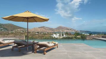 A poolside area with lounge chairs and an umbrella, overlooking a coastal landscape with mountains and buildings.