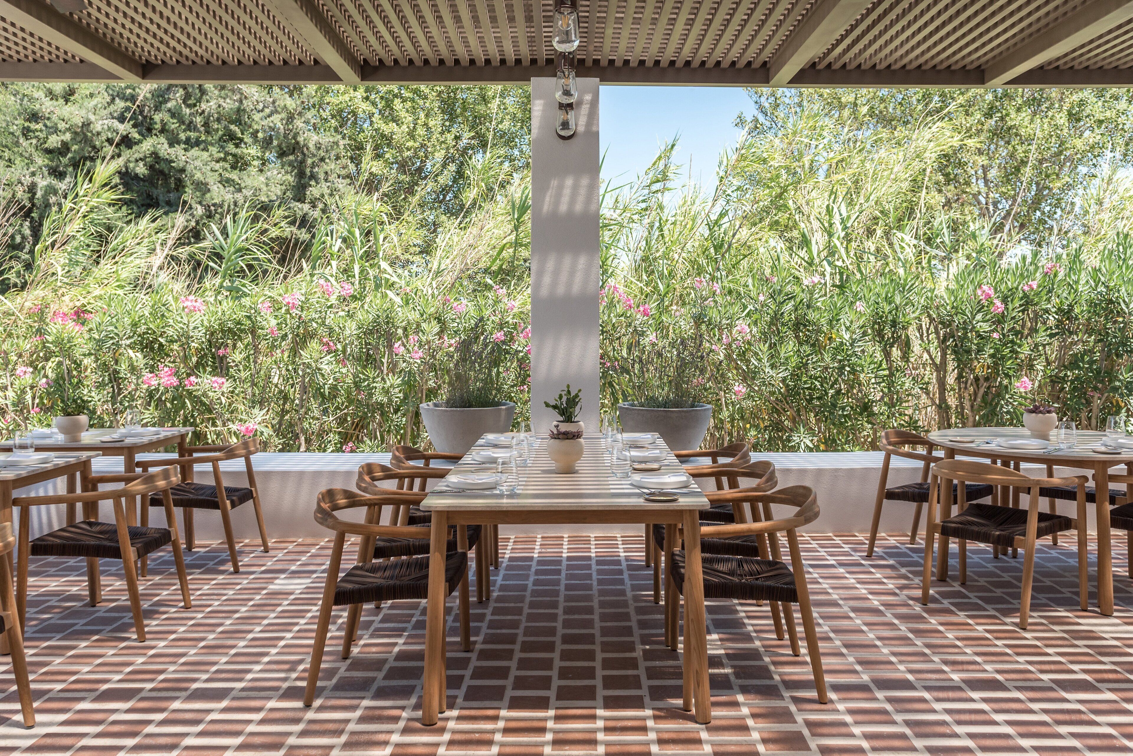 An outdoor dining area with a brick floor, wooden tables and chairs, and potted plants.