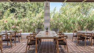 An outdoor dining area with a brick floor, wooden tables and chairs, and potted plants.