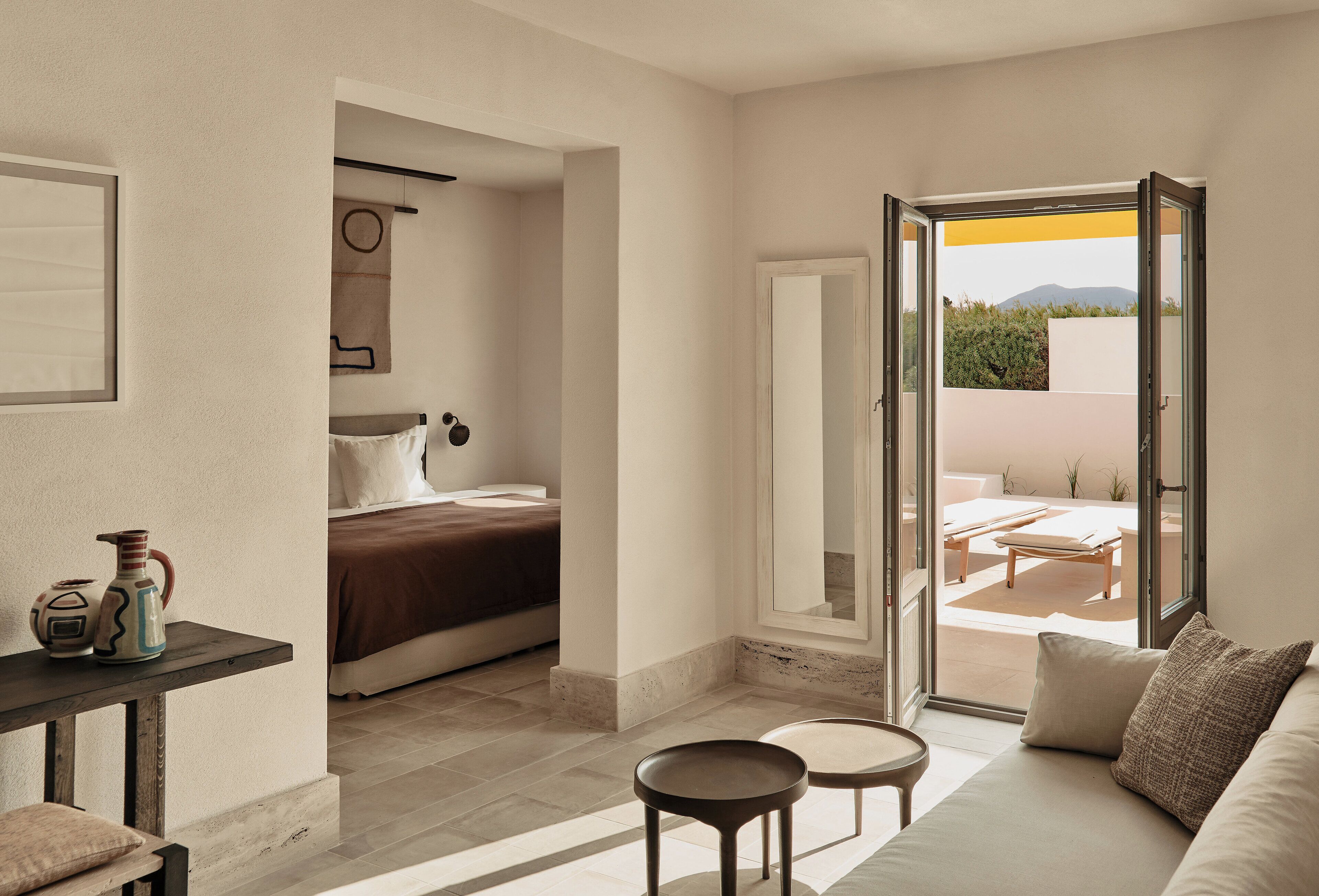 A modern hotel room with a bed, a small table, a sofa, and a balcony with outdoor furniture.