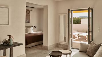 A modern hotel room with a bed, a small table, a sofa, and a balcony with outdoor furniture.