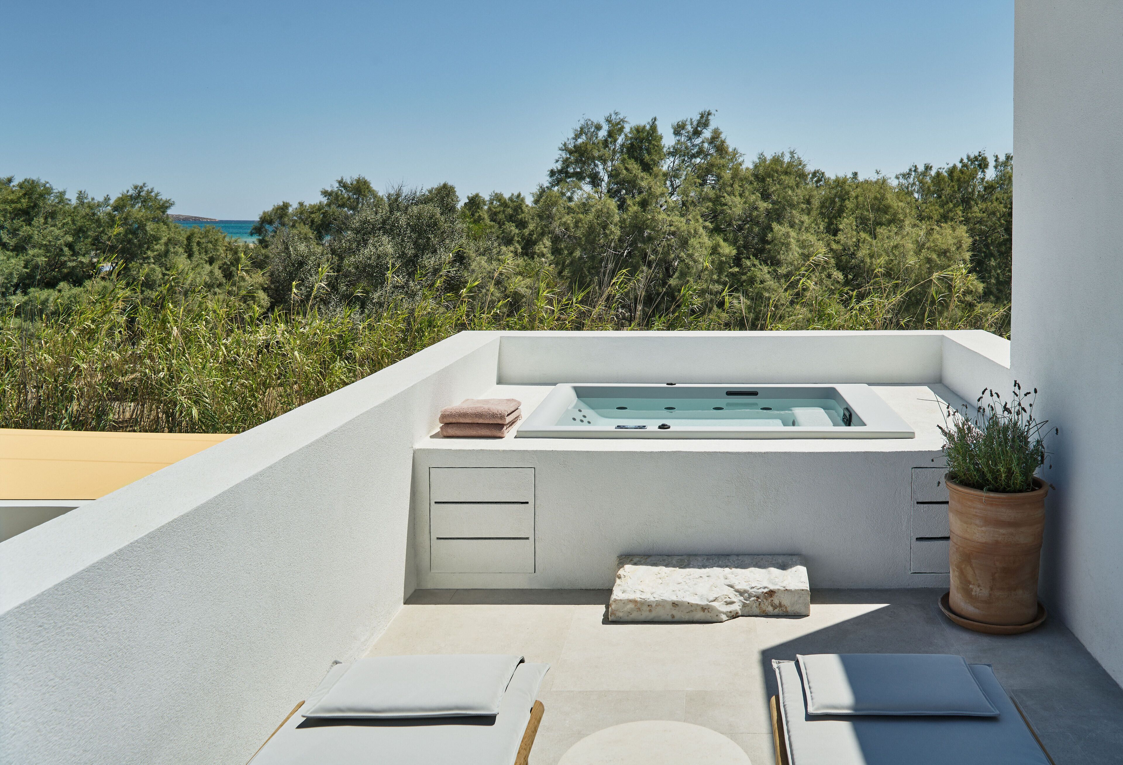 A modern outdoor bathroom with a bathtub, towels, and a potted plant.