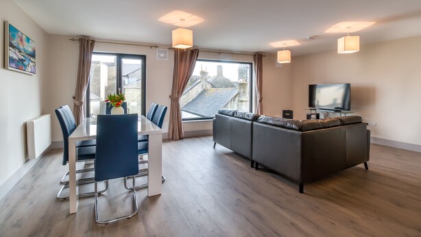 Un salon moderne comprenant un coin repas, un ensemble de canapés, un téléviseur et une grande fenêtre avec des rideaux.