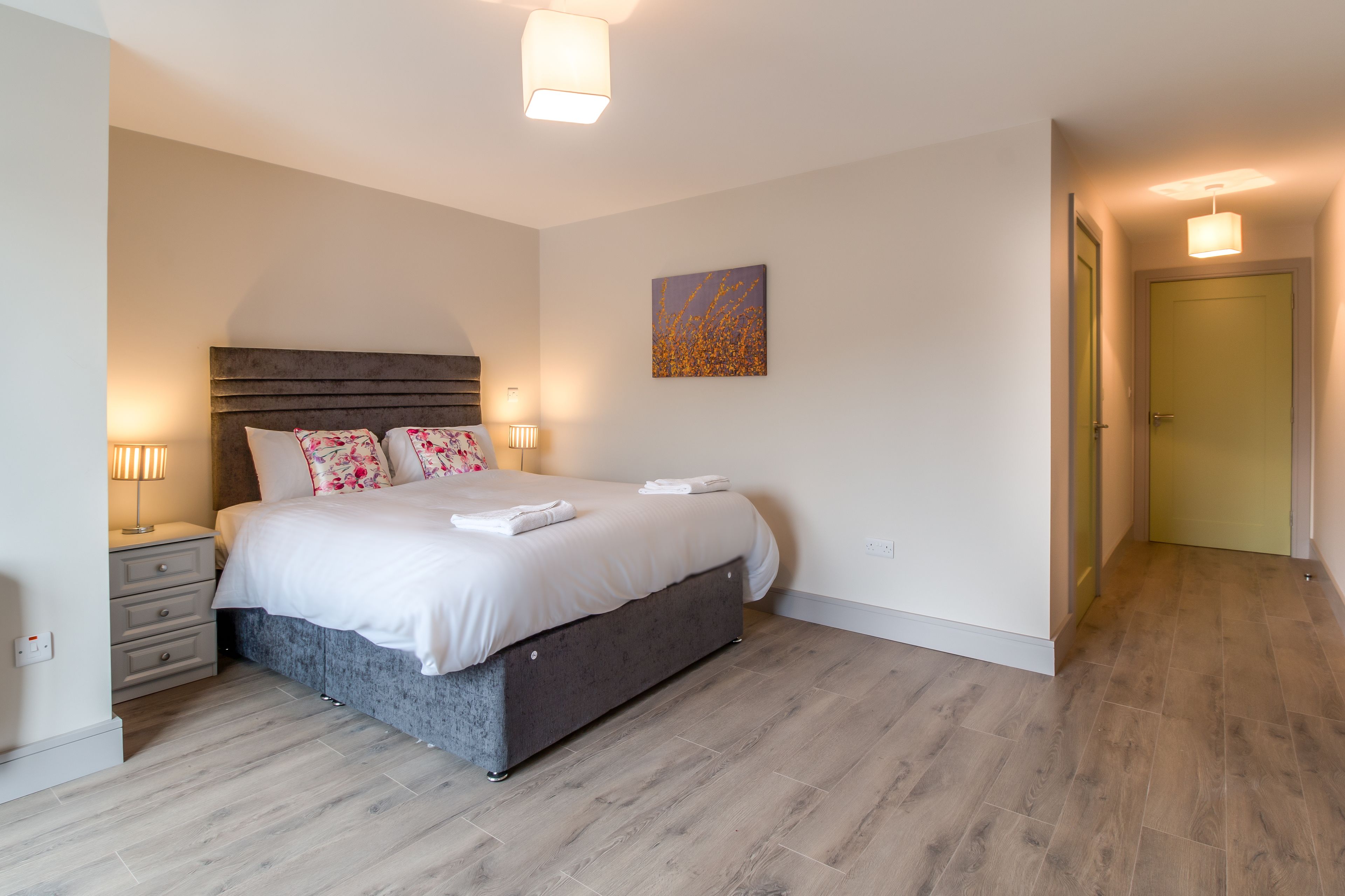 A modern bedroom with a bed, bedside tables, and a painting on the wall.