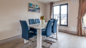 Un coin repas avec une table blanche et des chaises bleues, un vase rempli de fleurs et un tableau accroché au mur.