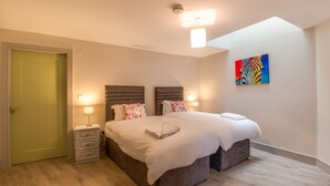 Une chambre avec deux lits, une table de chevet, une lampe et un tableau coloré au mur.