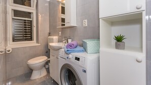 Un baño compacto con inodoro, lavadora, lavabo y un pequeño estante con una planta.