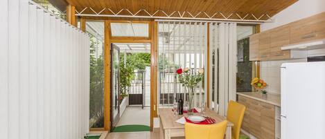 A dining area with a wooden ceiling, a yellow chair, a table with a red placemat, and a view of the outside through a glass door.