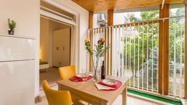 Un comedor con una mesa de madera dispuesta para dos personas, un florero con flores y vistas al jardín a través de una puerta corredera.