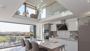 A modern kitchen with a central island, bar stools, a dining area with a view, and a built-in oven. - The Lookout - UKC3846 (Ticknall, near Derby)