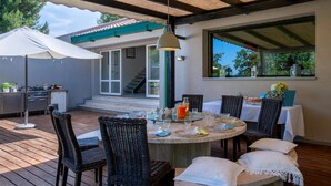 Une terrasse extérieure avec une table ronde dressée pour le repas, entourée de chaises en osier.