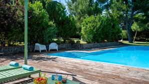 Une piscine avec une terrasse en bois, deux chaises blanches et une table sur laquelle sont disposés des bols remplis de nourriture.