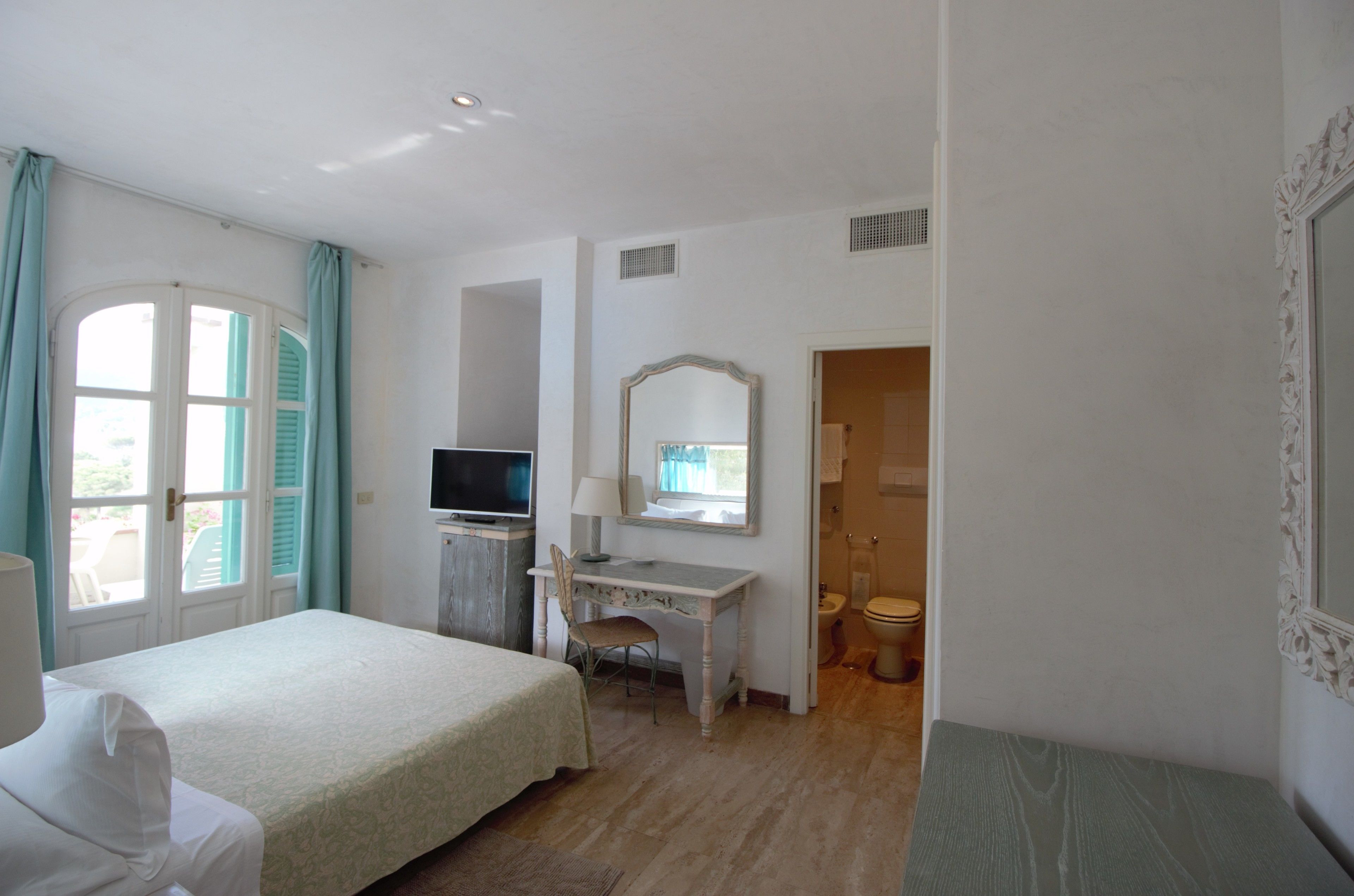 A hotel room with a bed, desk, chair, television, mirror, and bathroom.