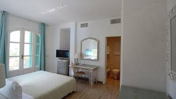 A hotel room with a bed, desk, chair, television, mirror, and bathroom.