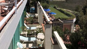 Ein Balkon mit Sitzgelegenheit im Freien, ein Pool und Blick auf das Meer und Boote.