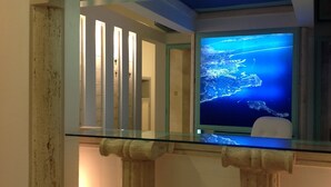 Ein Zimmer mit einem großen Aquarium, das eine Aussicht auf ein blaues Meer zeigt, einer Glastrennwand und einer Tür mit Schlüsselloch.