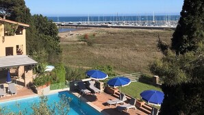 Ein Poolbereich mit Liegestühlen und Sonnenschirmen mit Blick auf einen Yachthafen und Boote.