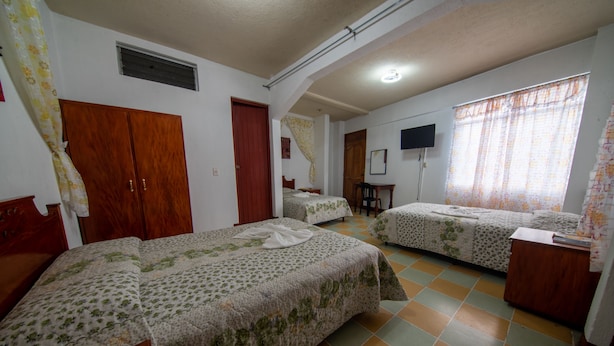 A bedroom with two beds, a wooden wardrobe, a desk, and a TV on the wall. - Hotel Casa Real (Quetzaltenango)