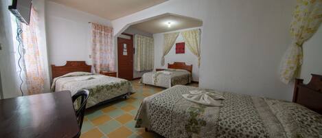 Quarto de hotel com três camas de solteiro, uma escrivaninha de madeira e uma cadeira.