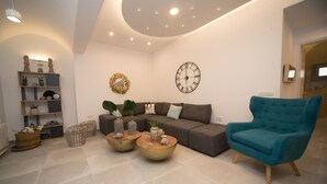 Uma sala de estar moderna com um sofá, duas mesinhas de centro redondas, uma poltrona azul, um relógio de parede e uma guirlanda decorativa.